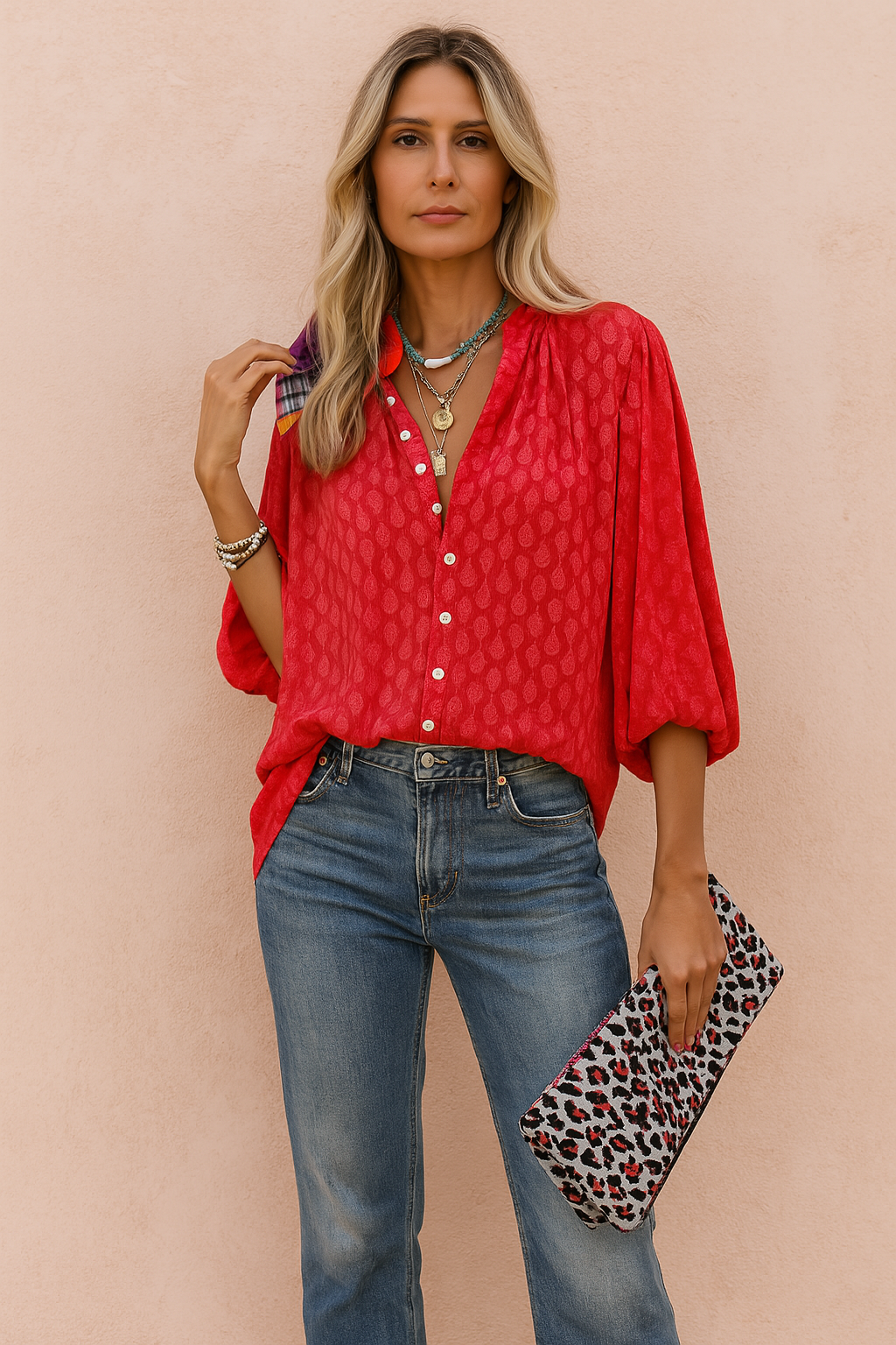 Stylish red jacquard blouse with subtle teardrop patterns, featuring a relaxed fit, mid-length puff sleeves, and white contrast buttons, paired effortlessly with vintage wash denim jeans and a statement leopard clutch.