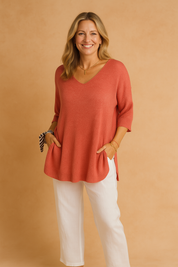 Loose-fit red knit tunic with a soft V-neckline and elbow-length sleeves, paired with straight-leg white linen trousers for a relaxed, elegant look.