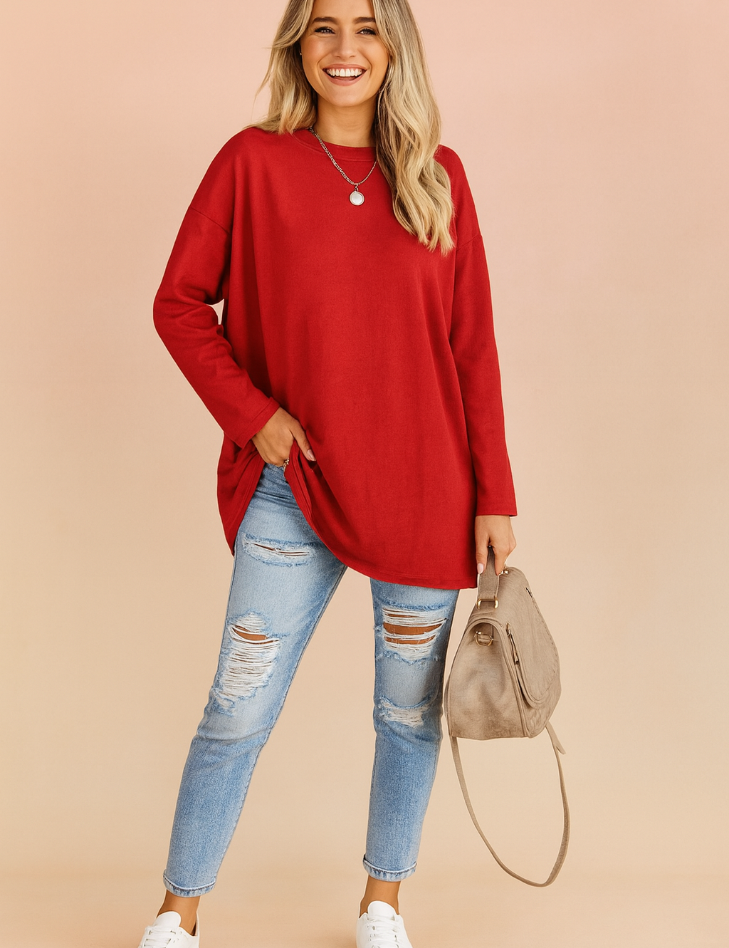 Long-sleeve oversized red top with a loose fit, paired with distressed light-wash skinny jeans and white sneakers, accessorized with a taupe handbag.