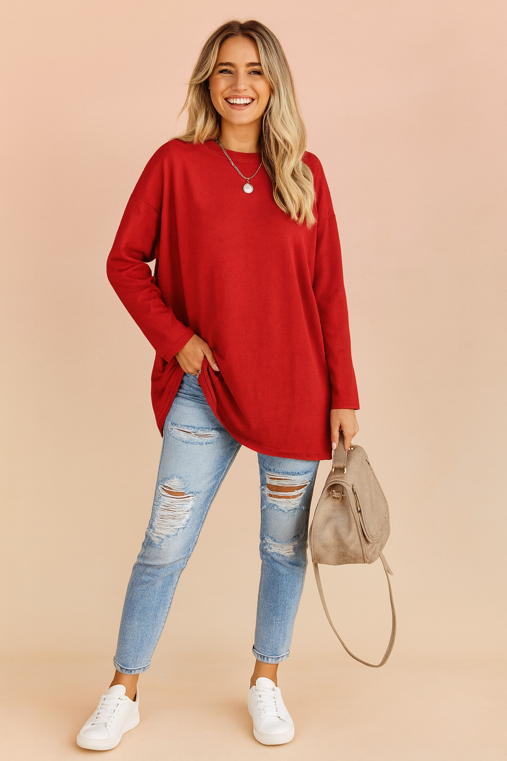 Long-sleeve oversized red top with a loose fit, paired with distressed light-wash skinny jeans and white sneakers, accessorized with a taupe handbag.