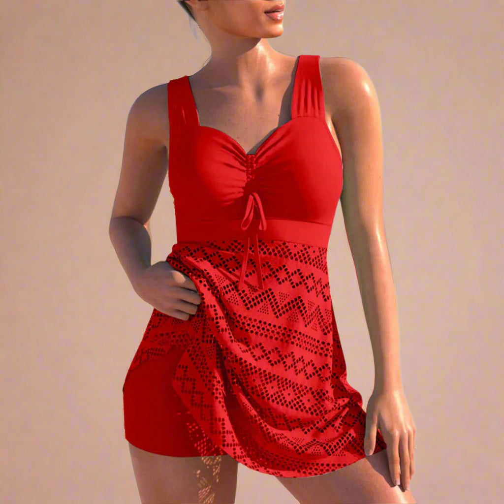 Stylish red swim dress featuring a ruched bust, wide shoulder straps, and a flattering waistband tie detail. The skirt is adorned with intricate geometric laser-cut patterns in matching red tones, creating a vibrant and eye-catching summer look.