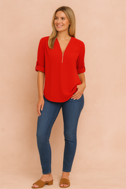 Bright red zip-neck blouse with roll-tab sleeves paired with fitted dark blue jeans and tan block-heel sandals.
