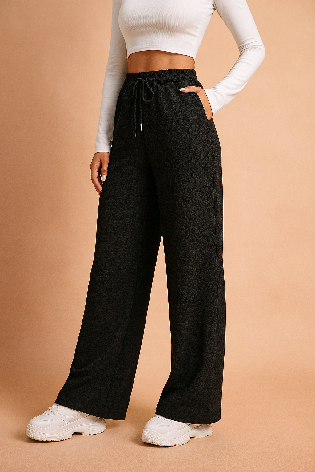 Wide-leg black lounge pants with an elastic drawstring waistband and side pockets, styled with white chunky sneakers and a long-sleeve fitted crop top.
