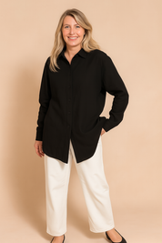 Long-sleeve black collared shirt with a relaxed fit, featuring a straight hem and front buttons, styled with high-waisted white wide-leg trousers and black ballet flats.