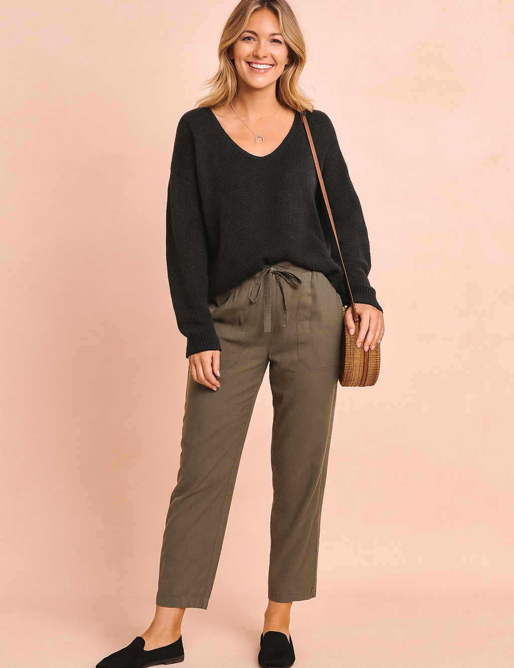 Black V-neck knit sweater paired with olive-green drawstring trousers, styled with black loafers and a woven rattan crossbody bag.