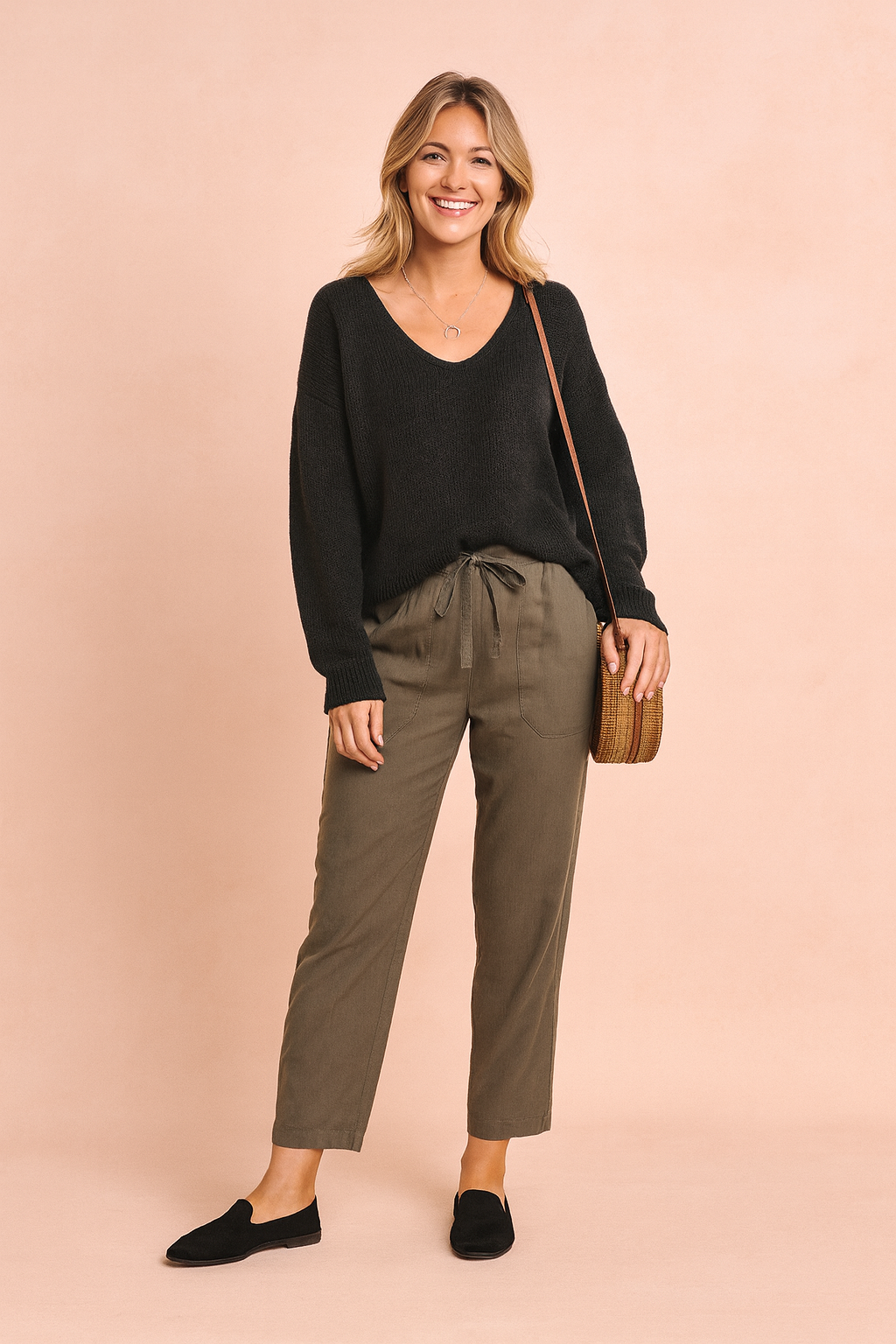 Black V-neck knit sweater paired with olive-green drawstring trousers, styled with black loafers and a woven rattan crossbody bag.
