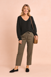 Black V-neck knit sweater paired with olive-green drawstring trousers, styled with black loafers and a woven rattan crossbody bag.