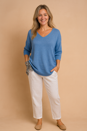 Women's lightweight blue V-neck knit sweater with three-quarter sleeves, paired with white linen trousers and a black-and-white striped scarf detail.