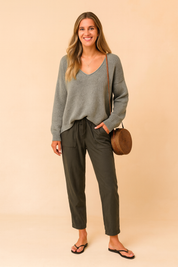 Relaxed-fit grey V-neck knit sweater paired with olive green drawstring waist pants and black flip-flop sandals, styled with a round rattan crossbody bag.