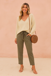 Cream knit V-neck sweater paired with olive green drawstring pants, complemented by beige block-heeled sandals and a round woven rattan crossbody bag.