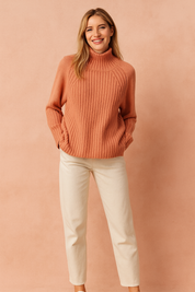 Cozy terracotta ribbed turtleneck sweater paired with straight-leg cream trousers and white sneakers, creating a relaxed yet stylish casual look.