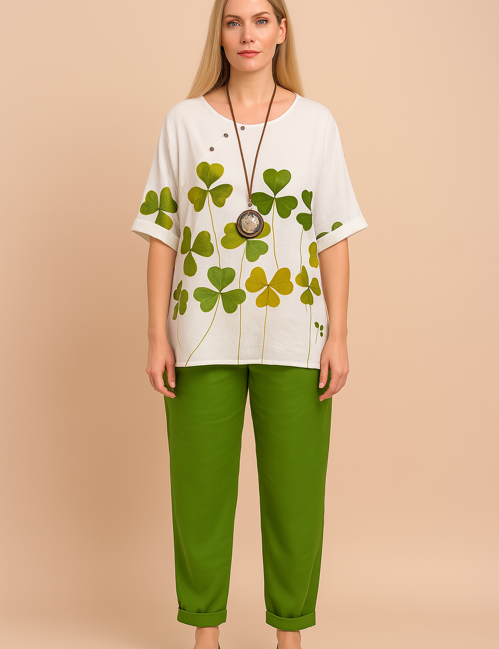 White oversized cotton top with green and yellow shamrock leaf print, featuring short cuffed sleeves, side slits, and a round neckline, paired with relaxed-fit ankle-length green trousers with tapered hem.
