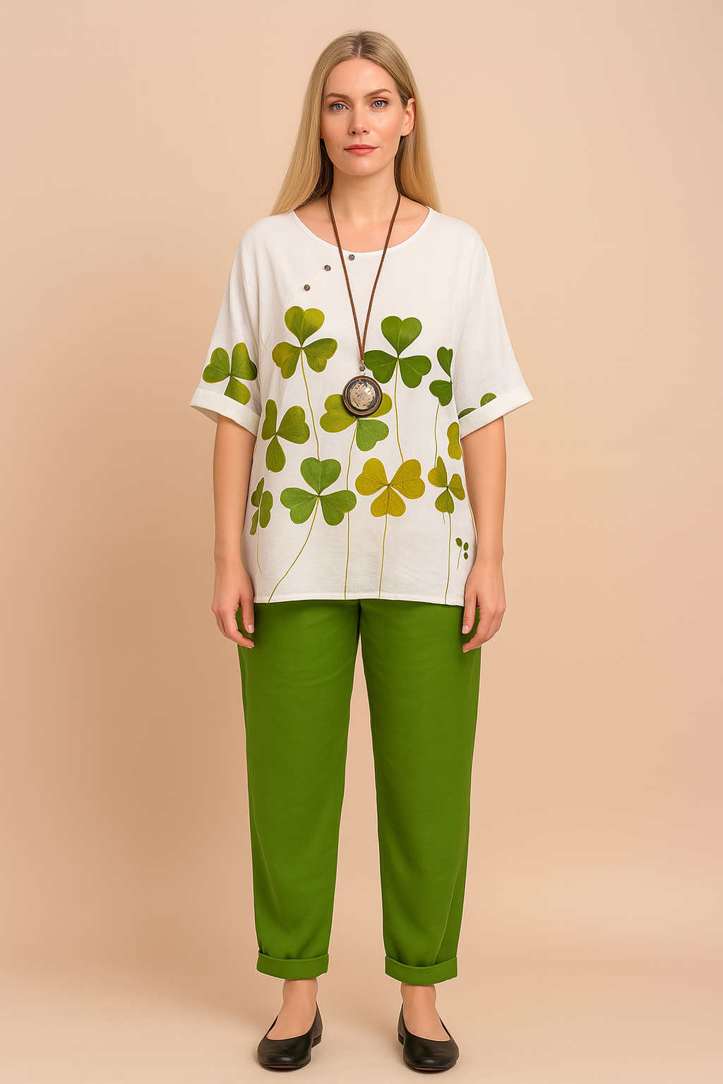 White oversized cotton top with green and yellow shamrock leaf print, featuring short cuffed sleeves, side slits, and a round neckline, paired with relaxed-fit ankle-length green trousers with tapered hem.