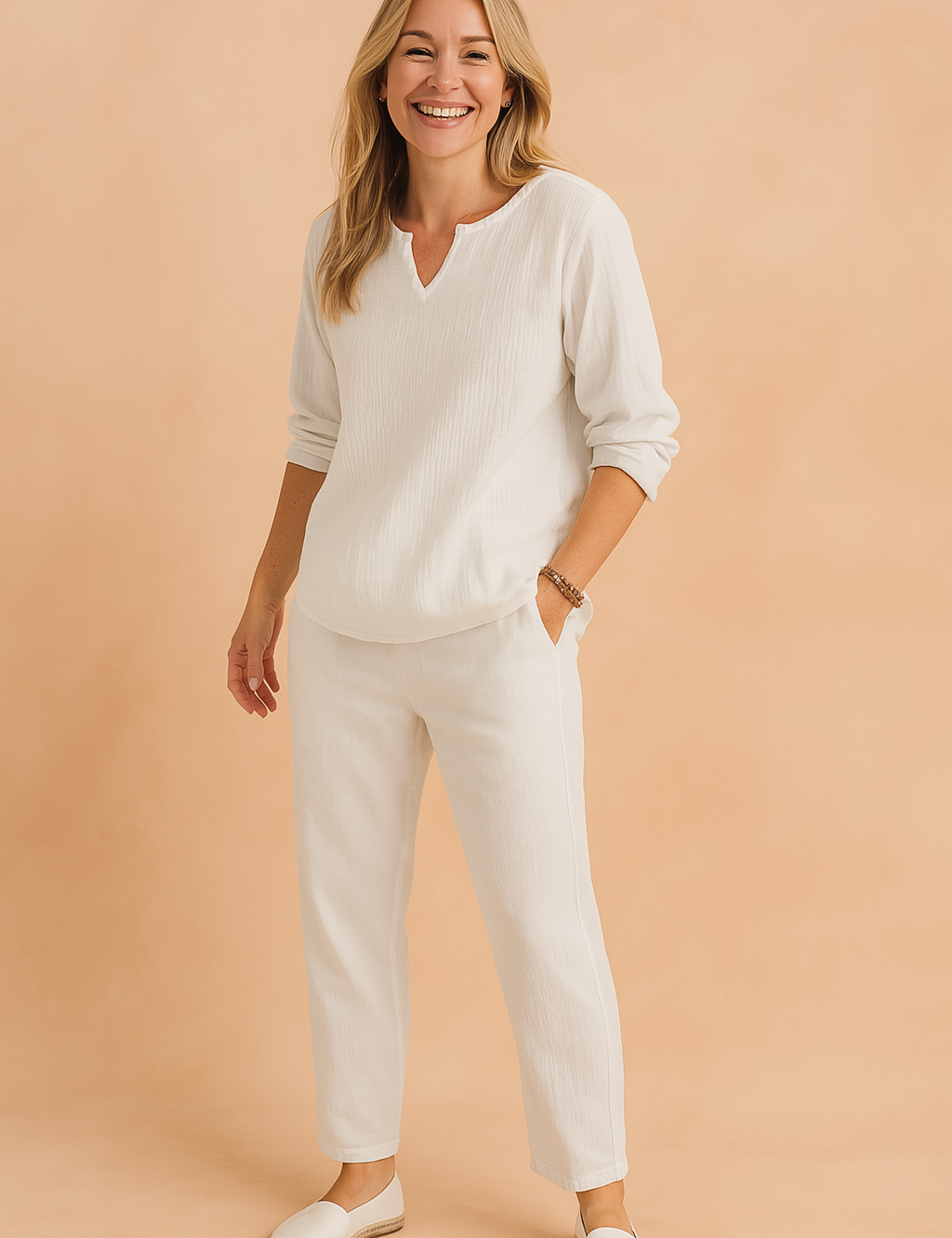Two-piece white textured cotton set featuring a relaxed-fit long-sleeve tunic top with a shallow V-notch neckline and matching tapered pants with side pockets, styled with minimalist white espadrilles for a clean, resort-ready look.