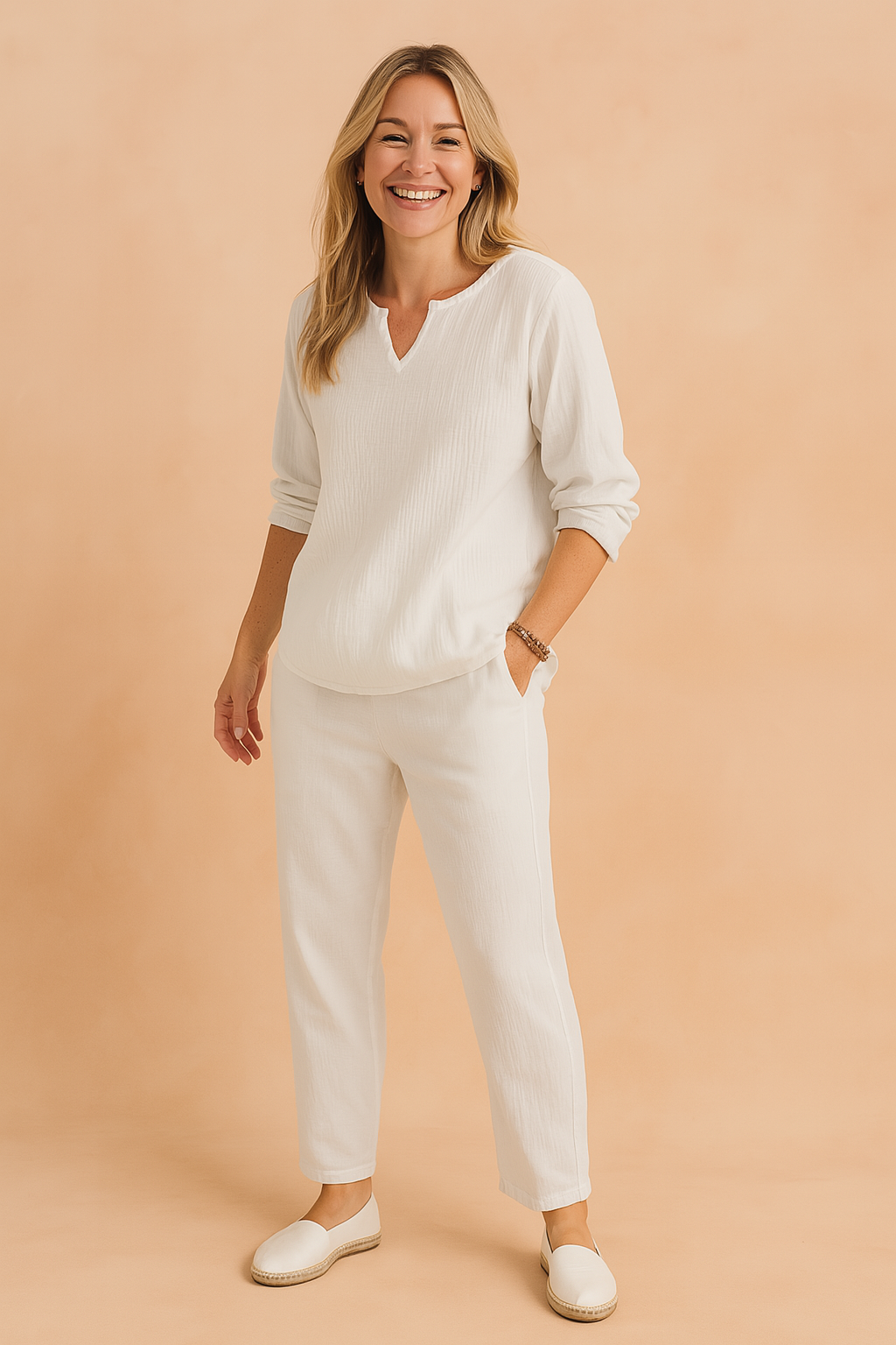 Two-piece white textured cotton set featuring a relaxed-fit long-sleeve tunic top with a shallow V-notch neckline and matching tapered pants with side pockets, styled with minimalist white espadrilles for a clean, resort-ready look.