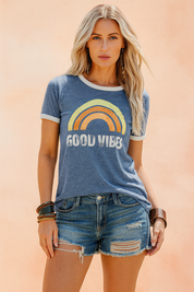Retro graphic tee in heathered blue featuring a distressed rainbow and "GOOD VIBES" print, styled with ripped denim shorts and bold bronze accessories, perfect for a laid-back, vintage-inspired summer outfit.