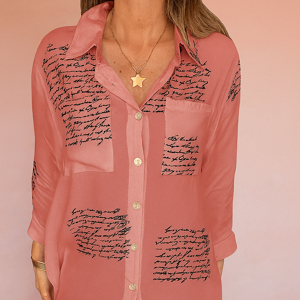 Flowy rose-pink button-down blouse with black handwritten script print on sheer fabric, featuring a relaxed collar, front buttons, and chest patch pocket detail.
