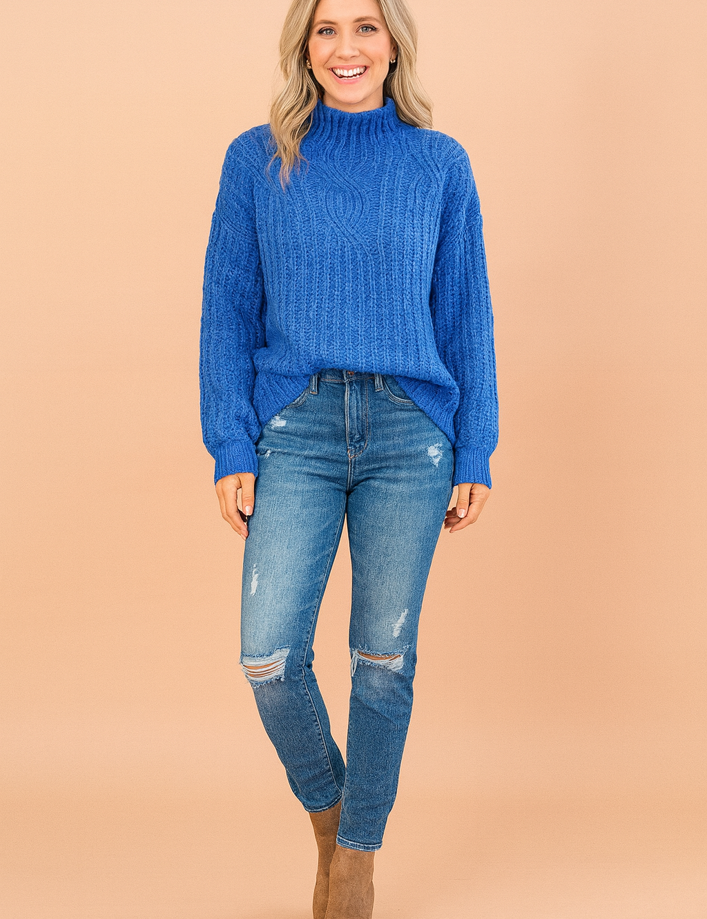 Royal blue cable-knit high-neck sweater paired with distressed blue skinny jeans and taupe ankle boots.