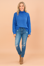 Royal blue cable-knit high-neck sweater paired with distressed blue skinny jeans and taupe ankle boots.