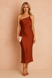 Elegant European woman with long ash blonde hair in a rust-colored satin midi dress, holding a clutch, standing against a softly lit warm sand and pastel pink background.