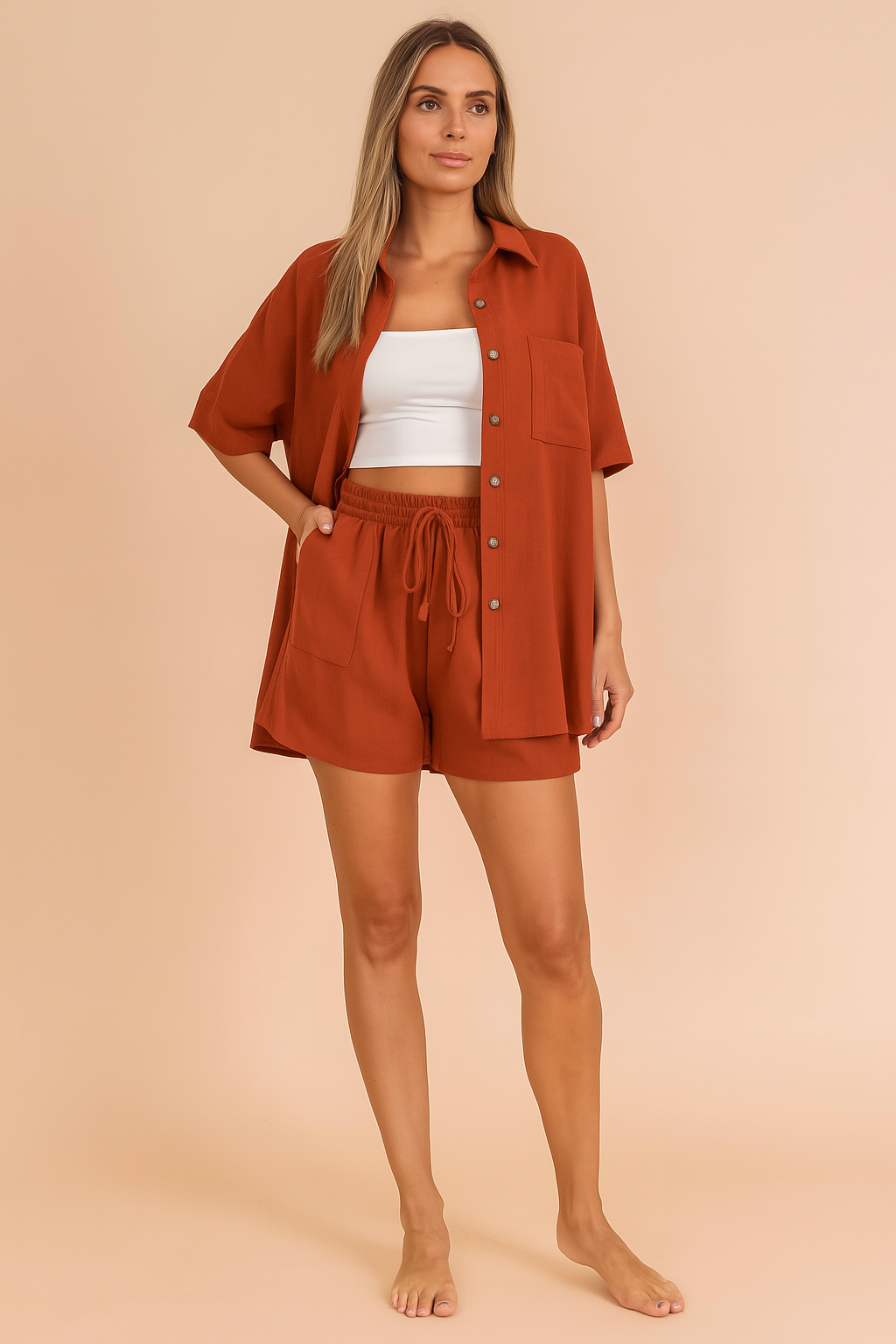 Rust orange button-down shirt and shorts co-ord set for women, featuring a relaxed fit and lightweight fabric, styled over a white crop top in a pastel blush fashion studio background.