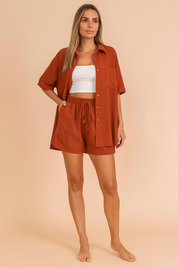 Rust orange button-down shirt and shorts co-ord set for women, featuring a relaxed fit and lightweight fabric, styled over a white crop top in a pastel blush fashion studio background.
