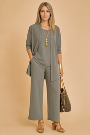 Elegant three-piece pantsuit featuring a draped longline cardigan, a matching loose-fit top, and wide-leg trousers in muted sage gray crepe fabric, styled with tan heeled sandals and accessorized with gold accents.