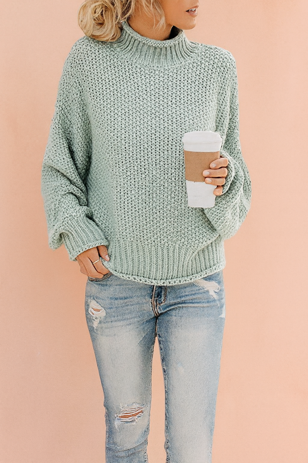 Light sage green chunky knit turtleneck sweater with ribbed cuffs and hem, paired with distressed light blue jeans.