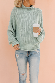 Light sage green chunky knit turtleneck sweater with ribbed cuffs and hem, paired with distressed light blue jeans.