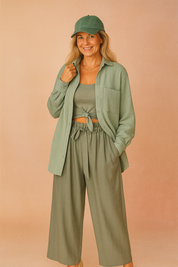 Light sage green textured button-up shirt layered over a matching knotted tank top, paired with wide-leg high-waisted sage trousers featuring a soft tie belt.