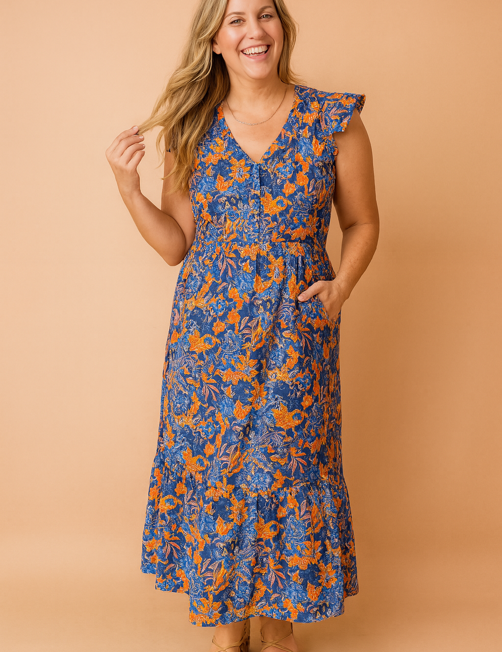 Flowy ankle-length blue and orange floral dress with flutter sleeves, a V-neckline, and a relaxed waistline, styled with strappy flat sandals.