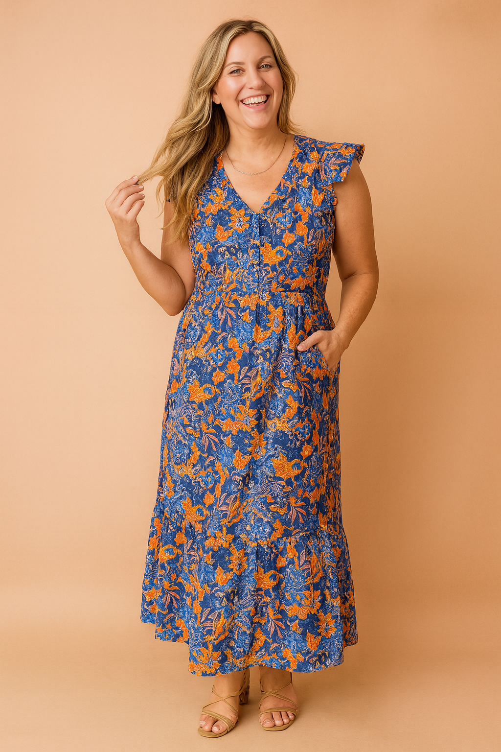 Flowy ankle-length blue and orange floral dress with flutter sleeves, a V-neckline, and a relaxed waistline, styled with strappy flat sandals.