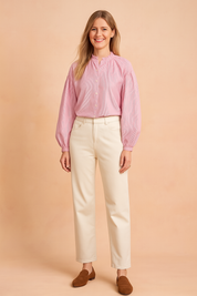 Pink and white vertical striped blouse with a gathered ruffle collar, front button closure, and long balloon sleeves, paired with high-waisted cream trousers and brown loafers.