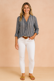 Vertical navy and white striped button-up blouse with rolled sleeves, styled tucked into high-waisted slim-fit white jeans with a brown belt and finished with tan flat slide sandals.