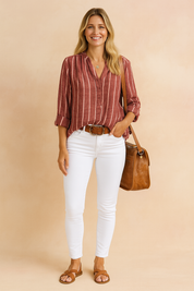 Burgundy and white vertical striped long-sleeve blouse with a buttoned V-neck and soft gathers at the shoulder seams, paired with fitted white high-rise pants, a tan leather belt, crossbody bag, and brown flat sandals for a polished casual look.