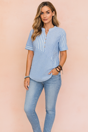 A stylish women's casual blouse featuring a unique mix of vertical and diagonal pinstripe patterns in soft blue tones, highlighted by wooden buttons and a curved hem, paired with light-wash fitted jeans in a pastel pink fashion studio backdrop.