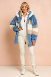 Striped faux fur hooded jacket in soft blue, beige, gray, and white tones, styled over a white quilted zip-up top with fitted cream leggings and lace-up ankle boots.