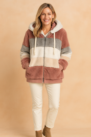 Striped faux fur hooded jacket with horizontal color blocks in dusty rose, light gray, off-white, and cream, paired with cream slim-fit pants and taupe ankle boots.