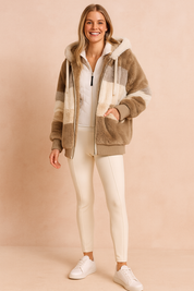 Striped faux fur hooded jacket in beige, cream, taupe, and gray tones paired with a white zip-up vest, slim-fit cream trousers, and white sneakers.