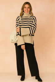 Beige and black striped turtleneck sweater with wide sleeves, paired with black wide-leg pants and black suede ankle boots, accessorized with an off-white tote bag.