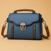 A structured blue handbag with brown accents and silver clasp, showcased against a pastel gradient background transitioning from pink to warm sand.
