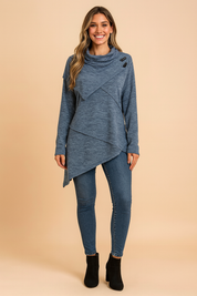 Long-sleeve heather blue asymmetrical tunic with cowl neck, decorative buttons, and layered hemline, paired with fitted medium-wash skinny jeans and black suede ankle boots.