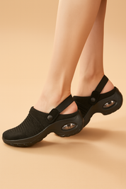 Black slip-on sandals featuring a breathable woven mesh upper, rounded toe, and wide black strap with button closure, paired with thick rubber soles and transparent air-cushion inserts in the heel for added support and shock absorption.