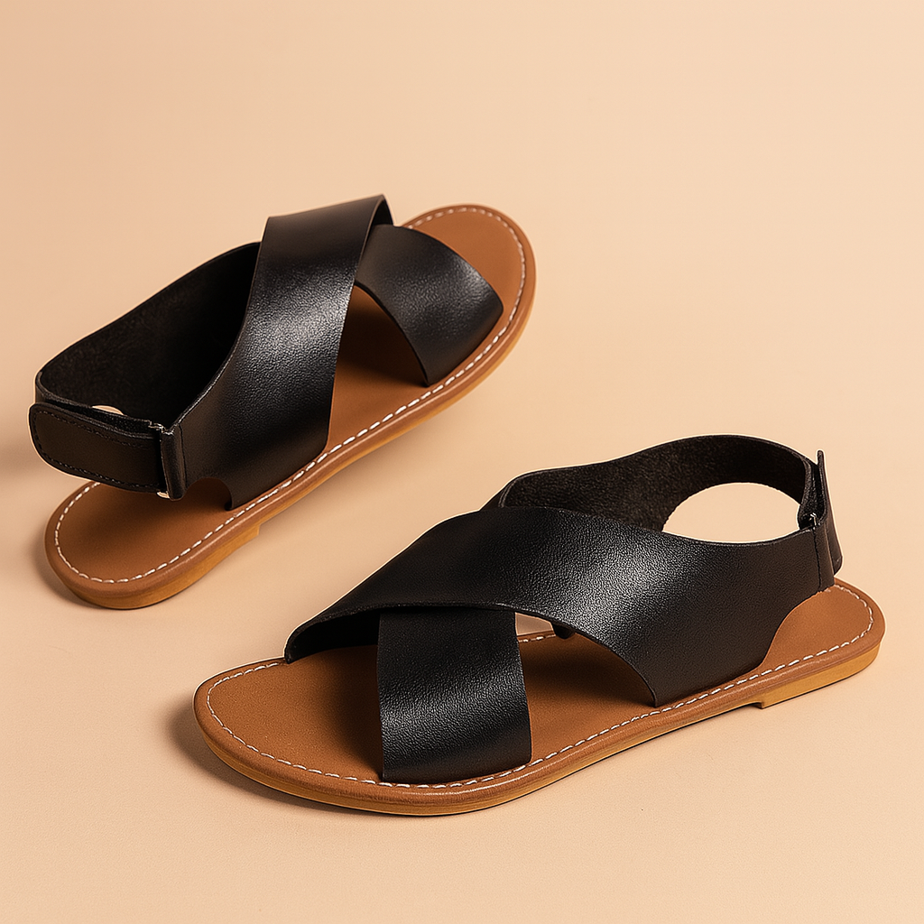 Women's black cross-strap flat sandals with a tan sole and decorative pearl zipper detail at the heel, crafted in a matte leather-like finish with white contrast stitching.
