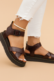  Dark brown faux leather platform sandals with black ridged soles, crisscross straps, yellow stitching, and a matte black buckle.