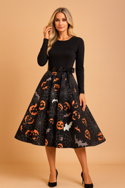 Sukienka halloweenowa retro z czarną górą z długim rękawem, satynową kokardą w talii i rozkloszowaną spódnicą ozdobioną nadrukiem pomarańczowych dyń, nietoperzy i pajęczyn na czarnym tle.