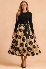Sukienka halloweenowa retro z czarną górą z długim rękawem, satynową kokardą w talii i rozkloszowaną złotą spódnicą ozdobioną nadrukiem czarnych dyń i pajęczyn.
