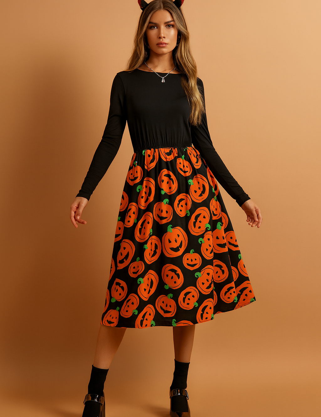 Sukienka halloweenowa z długim rękawem w kolorze czarnym z rozkloszowaną spódnicą midi ozdobioną pomarańczowym nadrukiem dyni z uśmiechniętymi twarzami.