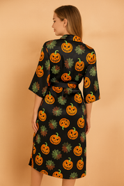 Satynowy szlafrok halloweenowy w kolorze czarnym z nadrukiem pomarańczowych dyń i kolorowych pajęczyn, wiązany w pasie z rozcięciem na nodze.