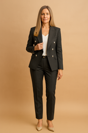 Tailored charcoal gray pantsuit with silver double-breasted buttons, structured lapels, flap pockets, and matching straight-leg trousers, styled with a white V-neck blouse and nude pointed-toe heels.